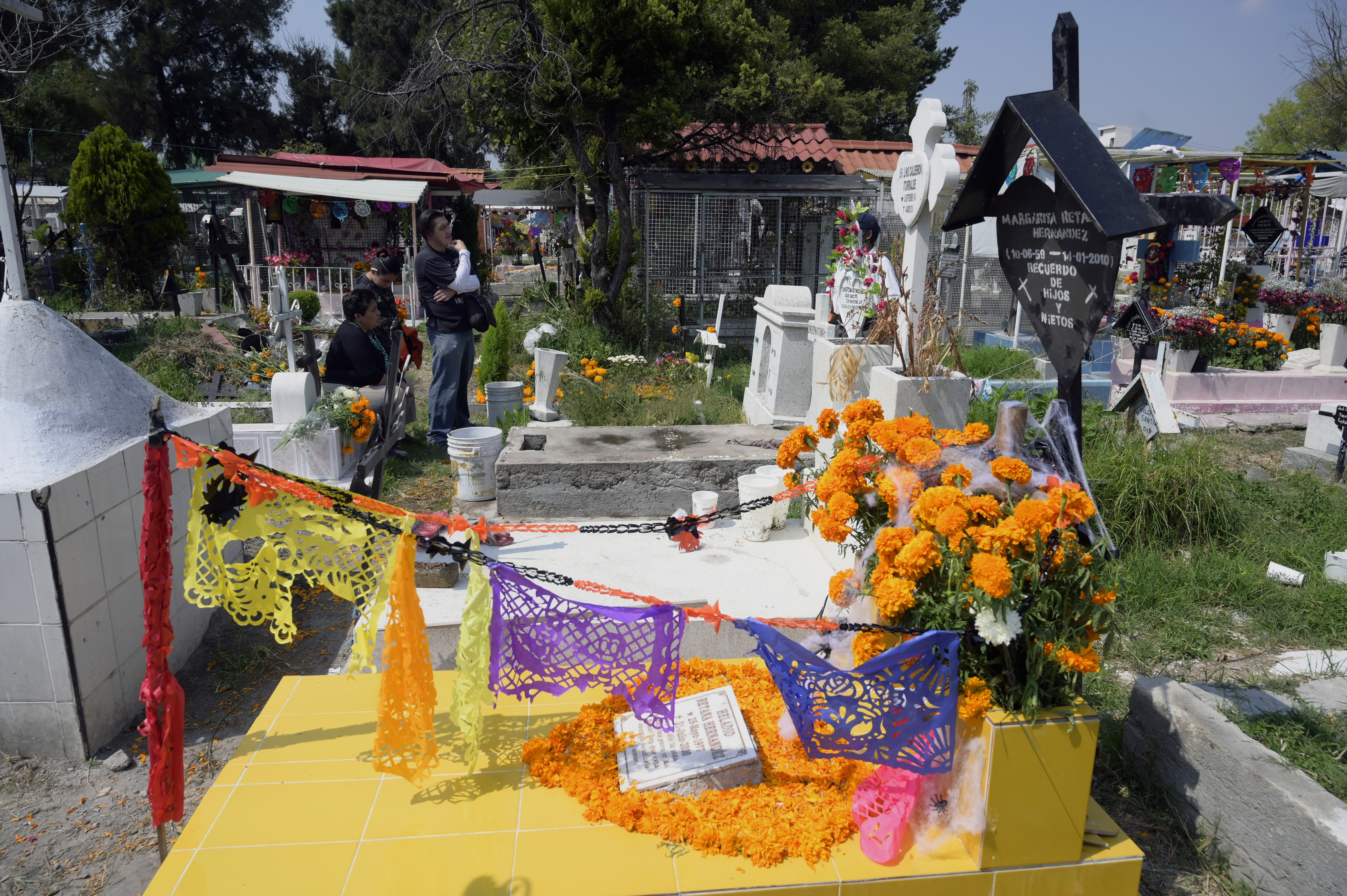 A family visit a relative's grave prior to the Day of the Dead at the Panteon San Jose, in Mexico City on October 28, 2020. - Due to the orange alert declared due to the Covid-19 pandemic, the authorities have decided to close the pantheons to visitors on November 1 and 2, the date that the dead are celebrated. (Photo by ALFREDO ESTRELLA / AFP)